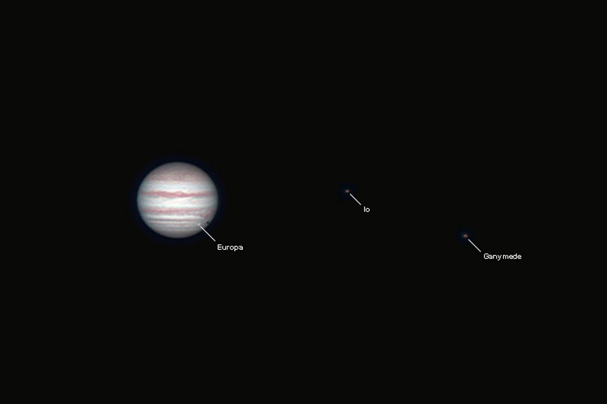 Image of the planet Jupiter, showing cloud belts, the great red spot, and three of the Galilean moons: Europa, which is transiting Jupiter's disc, Io, and Ganymede